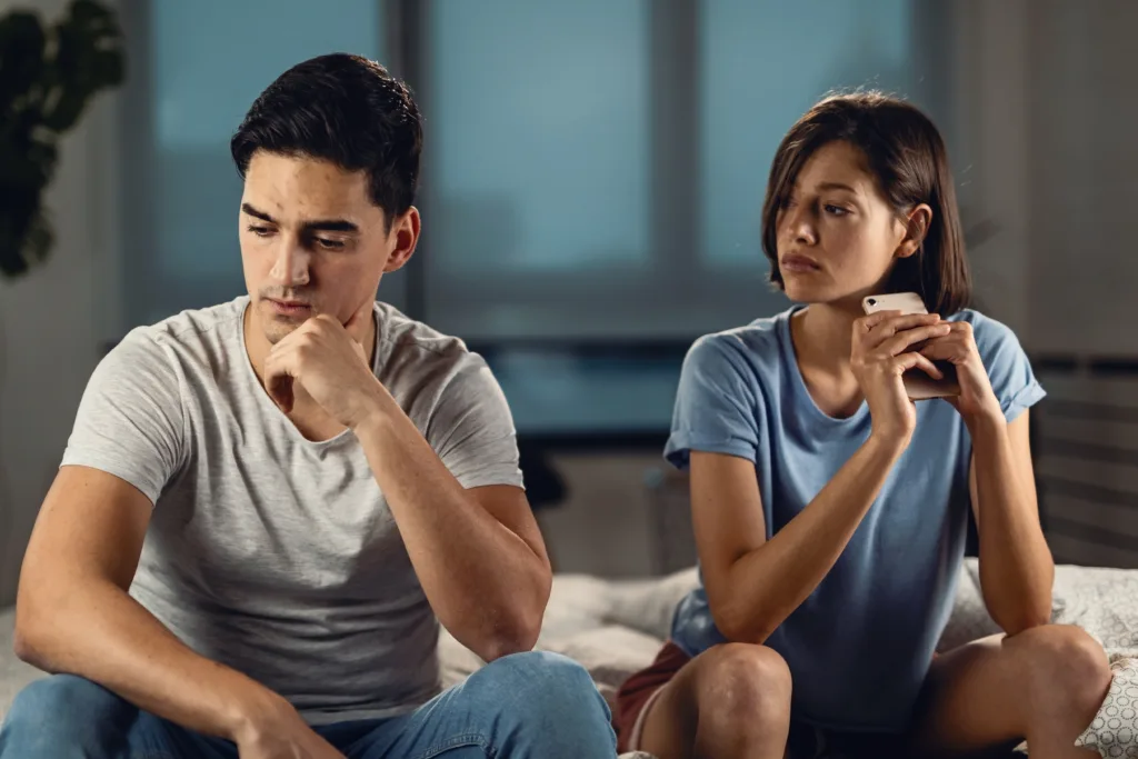 Young worried man thinking of something while sitting next to his girlfriend and having relationship problems with her.